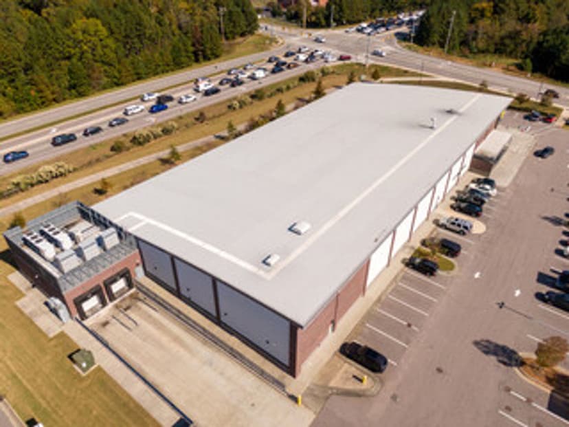 Aerial view of a large commercial building with a parking lot and nearby traffic.